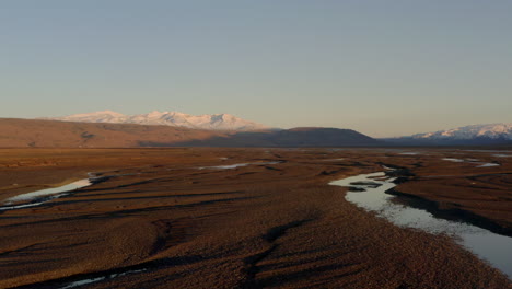 Low-slider-shot-over-icelandic-braided-rivers-with-highland-mountains-in-the-background