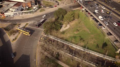 A-dynamic-aerial-shot-of-a-yellow-passenger-tram-crossing-the-road-towards-the-roundabout-arriving-to-the-subway-terminal
