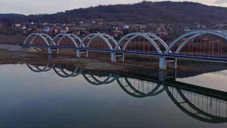 Eisenbahnbogenbrücke-Mit-Spiegelreflexion-Auf-Dem-Fluss-Mit-Stadthäusern-Im-Hintergrund