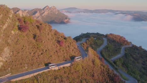 Tour-bus-with-tourist-driving-on-mountain-road-in-Italy-at-sunrise,-aerial