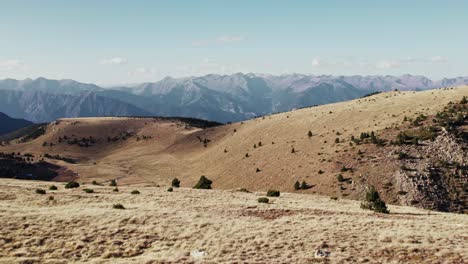 Aerial-drone-flying-over-dry-hill,-rocky-mountain-range-in-background-during-the-day