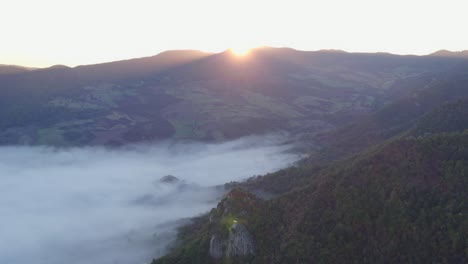 Sun-peaking-above-edge-of-mountains-during-sunrise,-mist-in-valley
