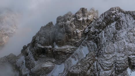 Aerial-top-down-shot-of-icy-mountains-on-mountaintop-surrounded-by-deep-clouds-at-sky