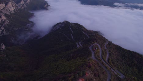 Winding-road-leading-down-into-clouds-at-Dolomiti-mountain-range,-aerial