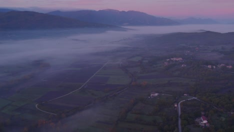 Italian-countryside-farm-land-covered-in-light-mist-during-sunrise,-aerial