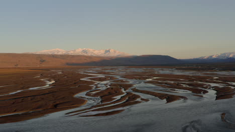 Aufsteigende-Luftaufnahme-über-Geflochtenen-Flüssen-Islands-Mit-Hochlandbergen-Im-Hintergrund