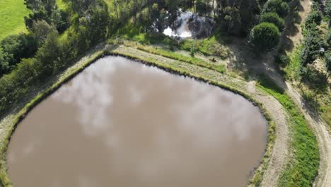 Drone-aerial-over-lush-land-and-dam-with-trees-in-country-town-Victoria