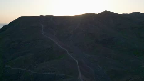 Aerial-shot-following-foot-trail-to-the-top-of-a-mountain,-revealing-the-beautiful-sunset