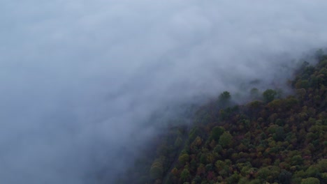 Cloudy-mist-edge-with-forest-mountain-slope,-aerial