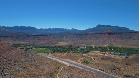 Drone-shot-of-road-running-through-Mount-Zion-with-a-mountain-range-in-the-background-located-in-Southern-Utah