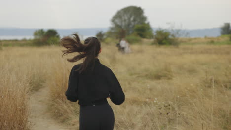 Rear-profile-of-a-athletic-Caucasian-woman-jogging-in-black-clothing-through-a-field-as-her-ponytail-bounces