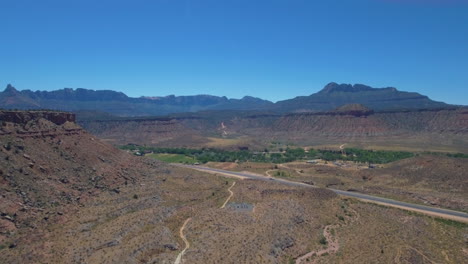 drone-shot-long-road-the-runs-through-Mount-Zion-with-Mountain-Range-in-the-background-located-in-Southern-Utah