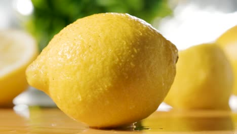 Frische-Zitrone-Fällt-Auf-Holztisch,-Zeitlupenaufnahme,-Verschwommene-Zitronen-Im-Hintergrund