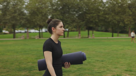 Athletic-fit-young-white-woman-in-black-yoga-attire-carrying-a-yoga-mat-through-a-public-park-in-Seattle,-Washington