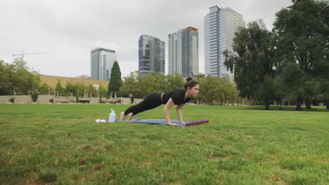 Forward-moving-shot-of-Caucasian-woman-doing-yoga-Chaturanga-dandasana-in-a-park-with-Seattle-skyline-in-background