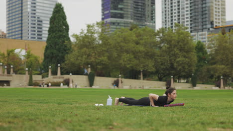 Beautiful-Caucasian-young-woman-performing-yoga-Chaturanga-Dandasana---plank-upward-dog---on-green-grass-in-a-Seattle-park