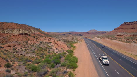 Ascending-drone-shot-starting-from-ground-level-to-200-feet-up-of-a-car-and-truck-driving-down-a-road-running-through-Mount-Zion-with-Mountain-range-in-the-background-located-in-Southern-Utah