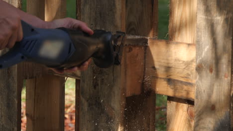 Close-up-of-man-using-reciprocating-saw-to-cut-through-panel-of-fence