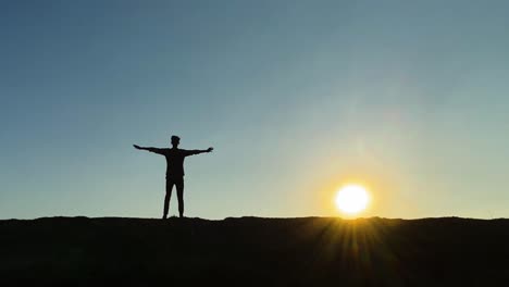 Silhouetted-young-man-doing-jumping-jacks-exercise-at-sunset