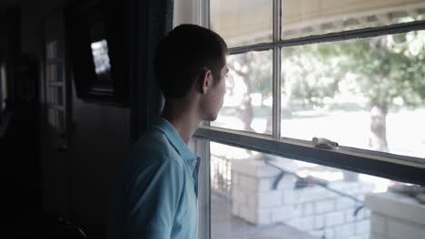 Young-man,-teenage-boy,-watches-out-window