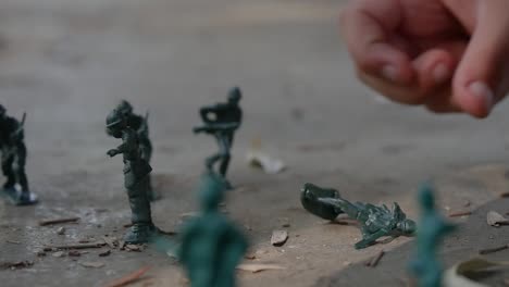 Close-up-of-a-child's-hands-playing-with-green-army-men-toys-in-the-sand