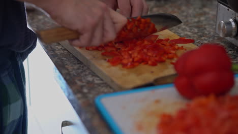 Closeup-of-man-hands-with-knife-cutting-fresh-red-pepper-on-wooden-board