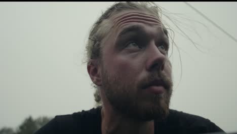 120-fps---Tired-and-sweaty,-young-caucasian-man-with-beard-and-ponytail-looking-up-at-mountain
