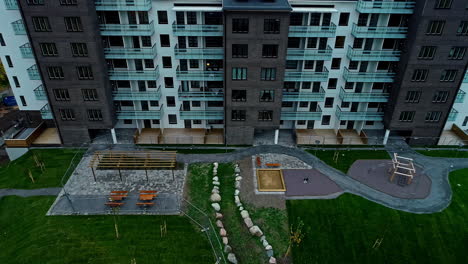 Exterior-View-Of-High-rise-Apartment-With-Playground-And-Green-Lawn-Outside-The-Building