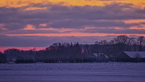 Sonnenuntergangszeitraffer-Des-Schneebedeckten-Feldes-Mit-Häusern-Und-Wald
