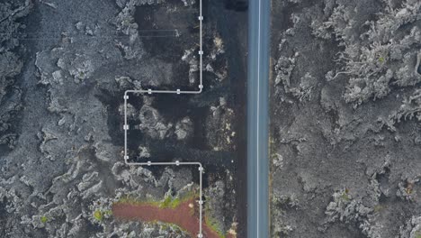 Pipe-line-carrying-hot-steam-geothermal-energy-along-road-in-Iceland,-top-down