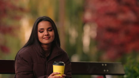 Beautiful-young-woman-with-her-eyes-closed-and-a-dreamy-smile,-enjoying-her-morning-coffee-in-a-park