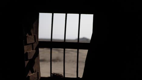 In-Einem-Dunklen-Raum,-Der-Durch-Metallstangen-Des-Fensters-Auf-Die-Trockene-Ländliche-Landschaft-In-Gwadar-Blickt