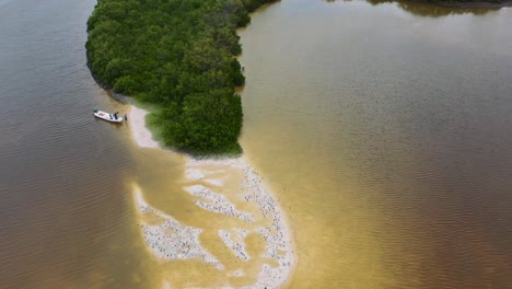 fishing-boat-docked-on-white-sand-beach-sandbar-surrounded-by-brown-river-in-Rio-Lagartos-Mexico,-aerial-to-down
