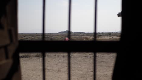 Looking-Through-Metal-Bars-Of-Window-Out-Towards-Arid-Rural-Landscape-In-Gwadar
