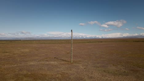 Wooden-power-pole-in-front-of-majestic-snow-capped-mountain-range-behind-dry-plains