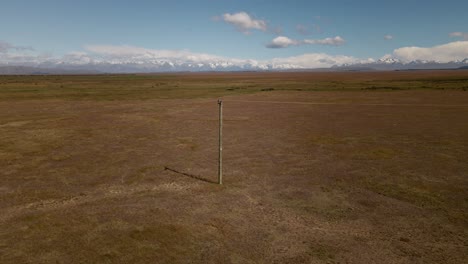 Wooden-power-pole-in-the-middle-of-endless-dry-plains-with-snow-capped-mountains-in-background