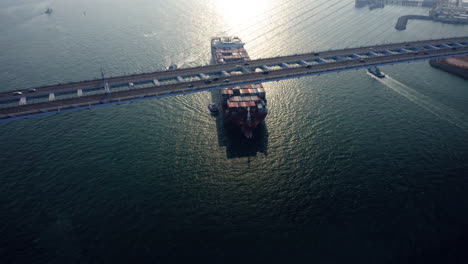 Giant-container-vessel-assisted-by-a-tugboat-setting-sail-to-open-sea-while-passing-the-Stonecutters-bridge-in-Hong-Kong