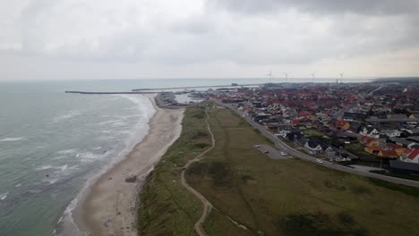Over-flight-of-Hirtshal-village-beach-coastline-on-cloudy-day-with-wind-turbines