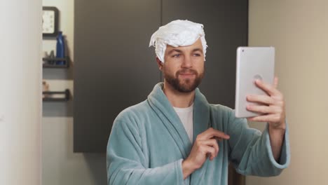A-cheerful-man-with-a-foam-hairstyle-takes-a-selfie-on-a-tablet
