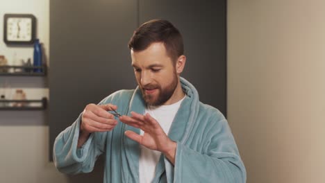 satisfied-man-is-doing-a-manicure-in-the-bathroom-wearing-a-bathrobe