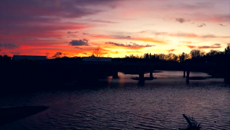 Autos,-Die-Flussbrücke-Mit-Schönem-Sonnenuntergang-Im-Hintergrund-überqueren