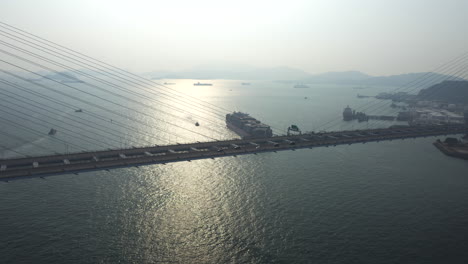 Autos-Fahren-über-Die-Breite-Hängende-Steinmetzbrücke-Mit-Tollem-Blick-Auf-Den-Rambler-Channel,-Wo-Ein-Großes-Containerschiff-Bei-Sonnenuntergang-In-Den-Hafen-Von-Hongkong-Einfährt