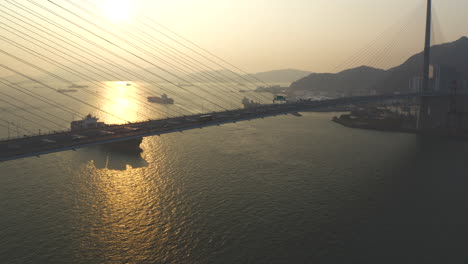 Container-ship-approaching-the-port-of-Hong-Kong-behind-suspension-bridge-during-golden-hour