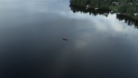 Aerial,-small-personal-fishing-boat-in-the-middle-of-a-calm-lake-in-the-early-morning