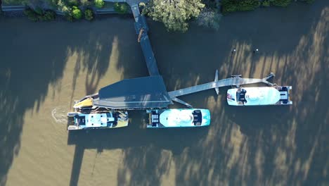 Zeitraffer-Drohnenaufnahme-Von-Oben-Nach-Unten-Von-2-Cat-Booten-In-Der-Stadt,-Die-Das-Dock-Verlassen-Und-Auf-Dem-Fluss-Davonfahren