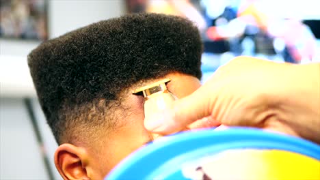 Nahaufnahme-Einer-Statischen-Aufnahme-Eines-Friseurs,-Der-Einen-Haarschnitt-Auf-Einem-Afroamerikanischen-Jungen-Mit-Goldenen-Akku-Trimmer-Oder-Haarschneidemaschinen-Ausrichtet