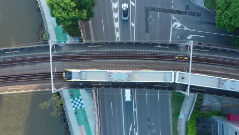 Top-down-stationary-drone-shot-of-train-passing-above-busy-road