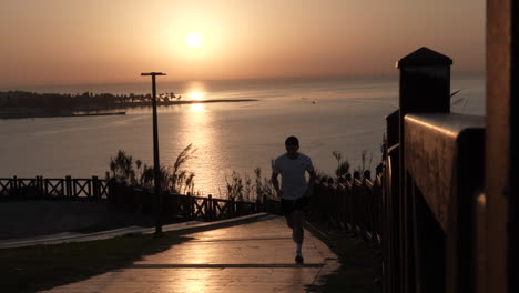 Silhouette-of-Man-Running-Uphill-With-Sunset-Above-Sea-in-Background,-Slow-Motion