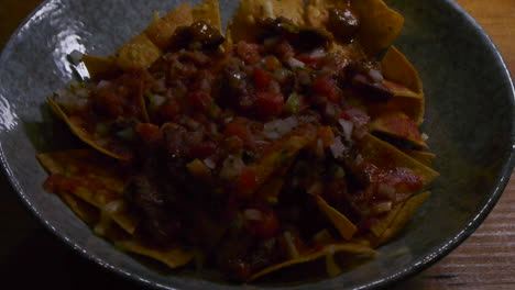 Bowl-of-nachos-topped-with-spicy-salsa-and-minced-meat,-filmed-as-close-up-with-light-movement-to-reveal-dish