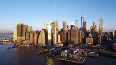Ascending-aerial-view-in-front-of-the-golden-hour-lit-skyline-of-Lower-Manhattan,-NYC